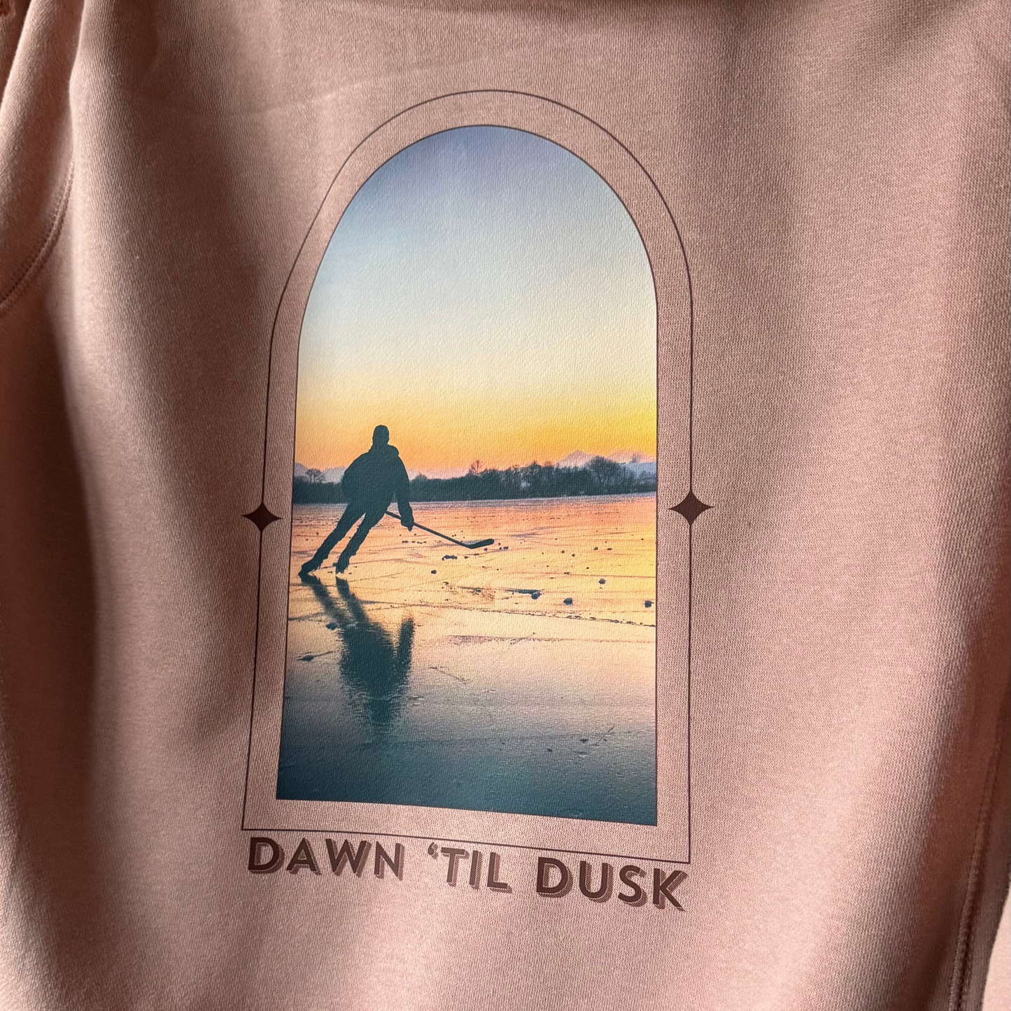 Pink hoodie with a graphic of a person walking on a beach at sunset and text 'Dawn 'Til Dusk'.