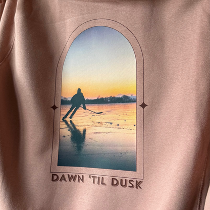 Pink hoodie with a graphic of a person walking on a beach at sunset and text 'Dawn 'Til Dusk'.