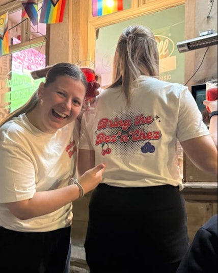 Two people wearing matching shirts with text, standing in a casual setting.